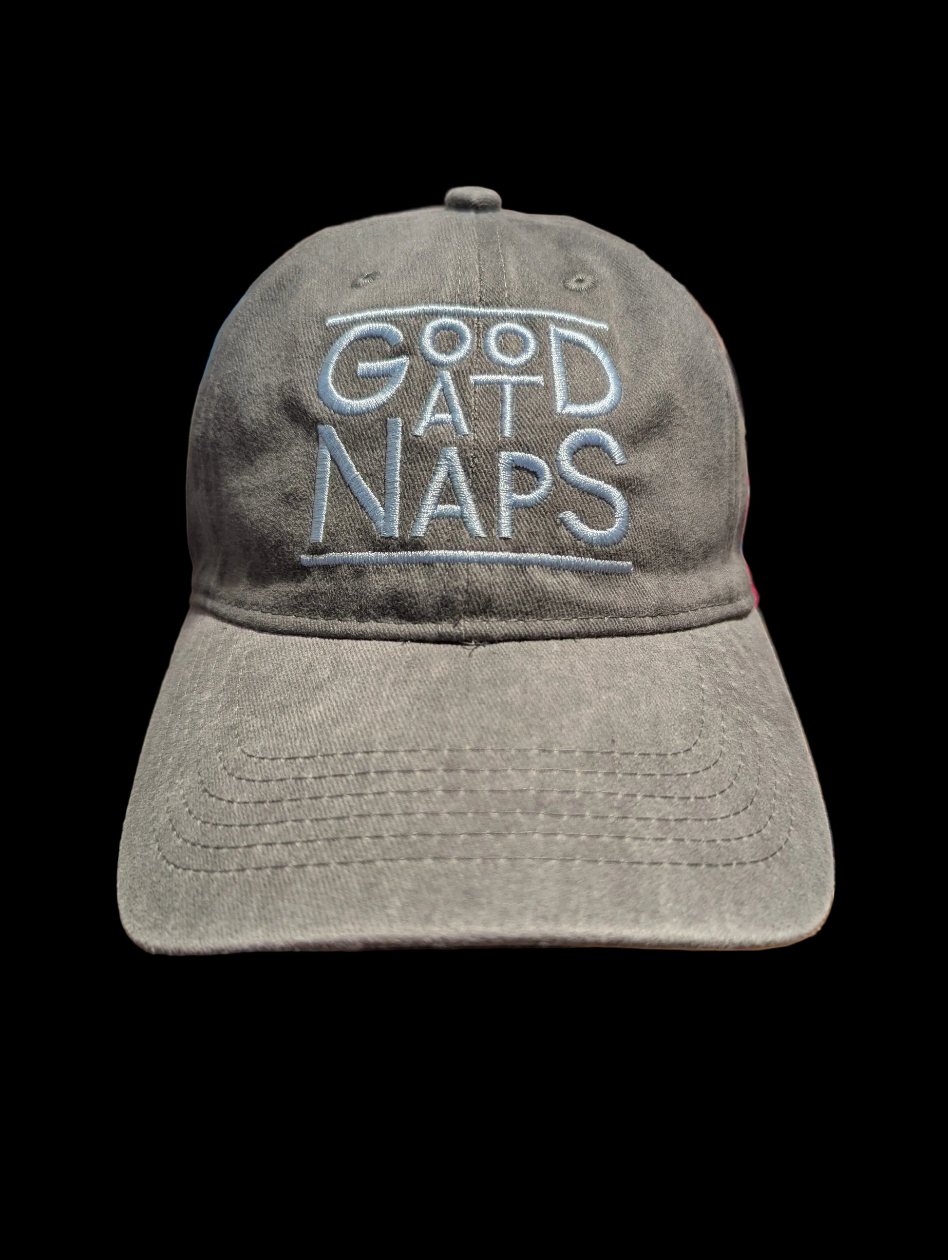 A gray washed baseball cap with 'GOOD AT NAPS' embroidered in light blue on the front