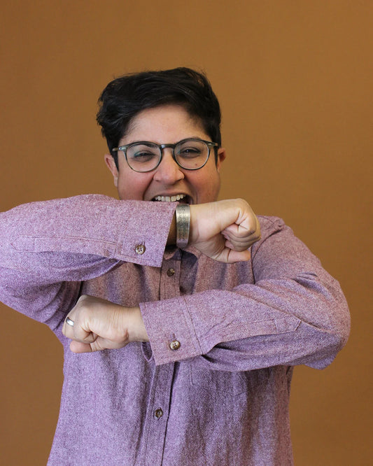 Person wearing a purple shirt with rolled-up sleeves against a brown background